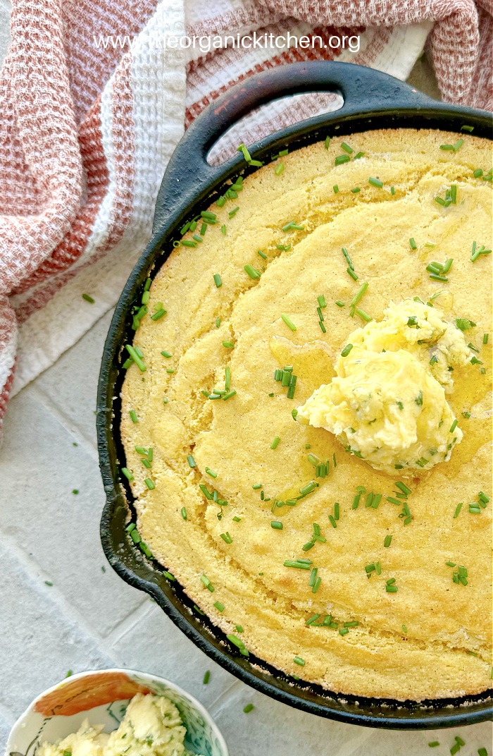Buttermilk Cornbread with Chive Honey Butter in black skillet set on gray bricks with red ans white dish towel in background