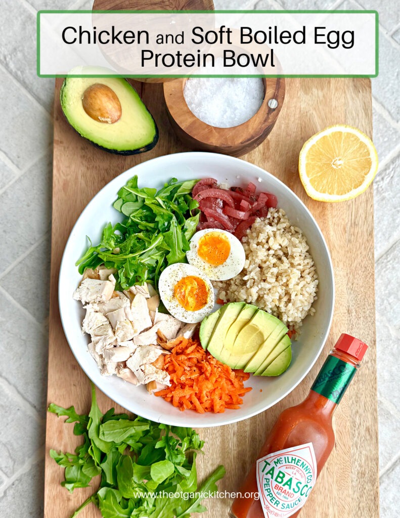 A white bowl set on wood platter with rice, chicken, arugula, and onions surrrounded by a bowl of salt. hot suace, lemon wedge and dish towellr