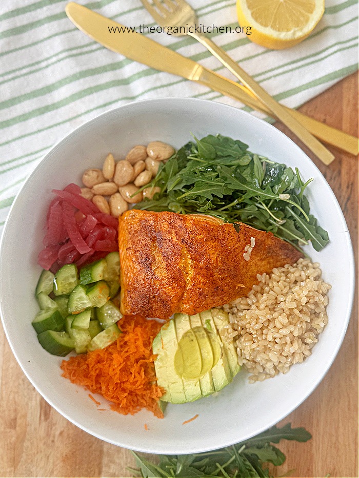 Easy Salmon Protein Bowl in white bowl on wood platter, with dish towel, gold utencils, and lemon wedge