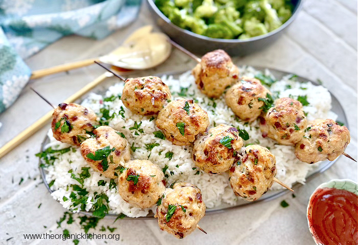 Bacon Sriracha Chicken Skewers and Coconut Rice Bacon Sriracha Chicken Skewers and Coconut Rice on platter with gold utencils and bowl of broccoli in the background
