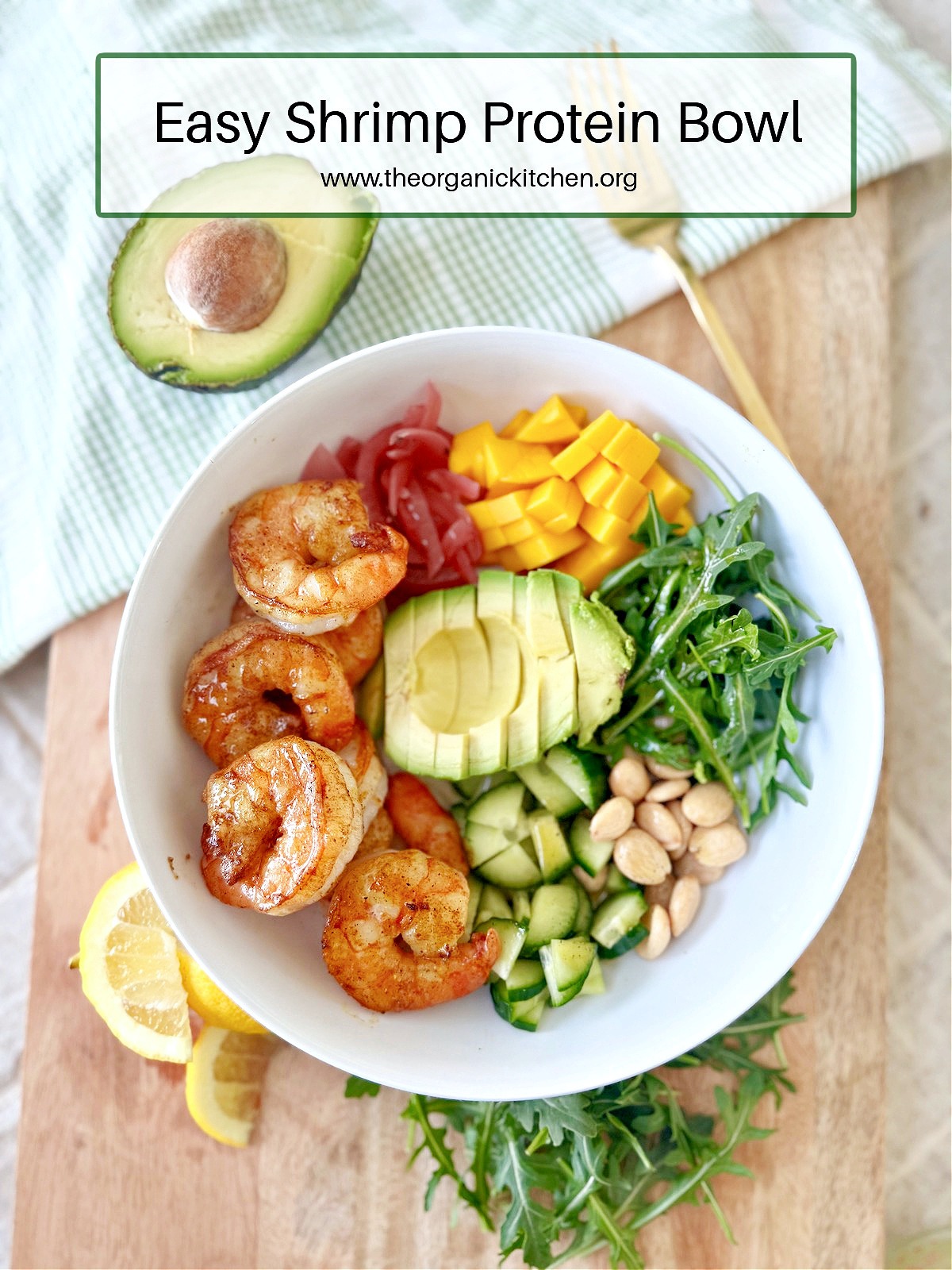 Easy Shrimp Protein Bowl in a white plate set on a wooden platter, surrounded by half and avocado, lemon wedges, and a gold fork