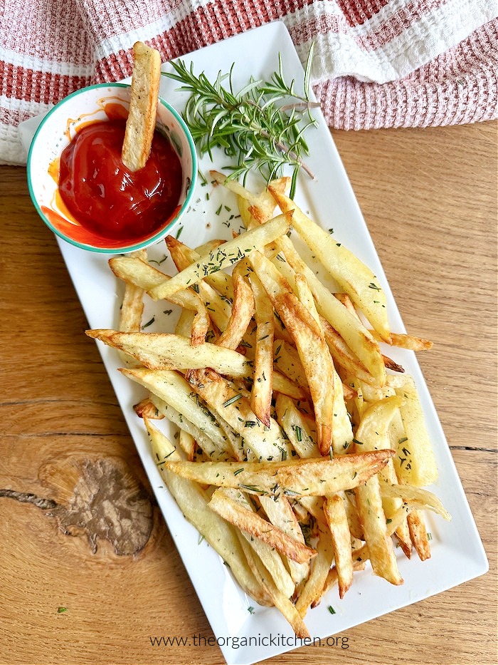 Air Fryer French Fries (Whole30) on white dish with small bowl of ketchup and dish towel in the background