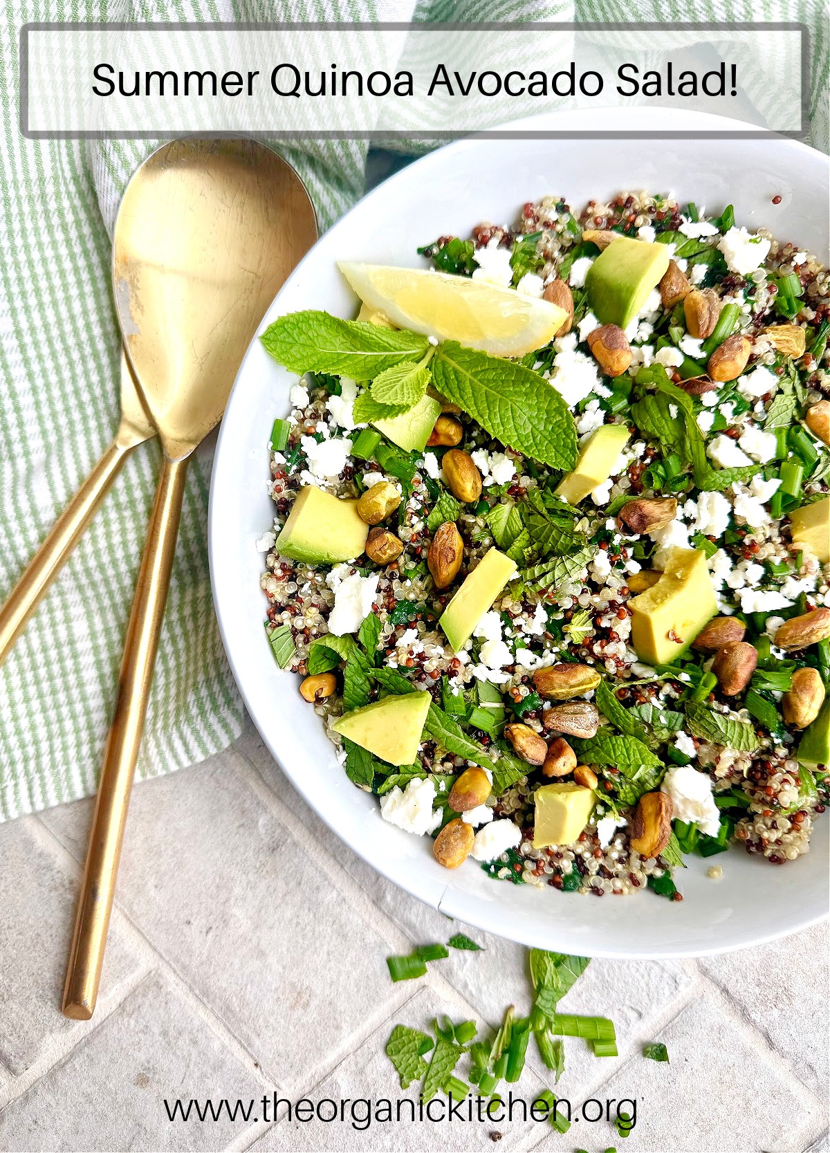 Quinoa Avocado Salad in a white bowl with gold serving spoons and green and white dishtowel in the background