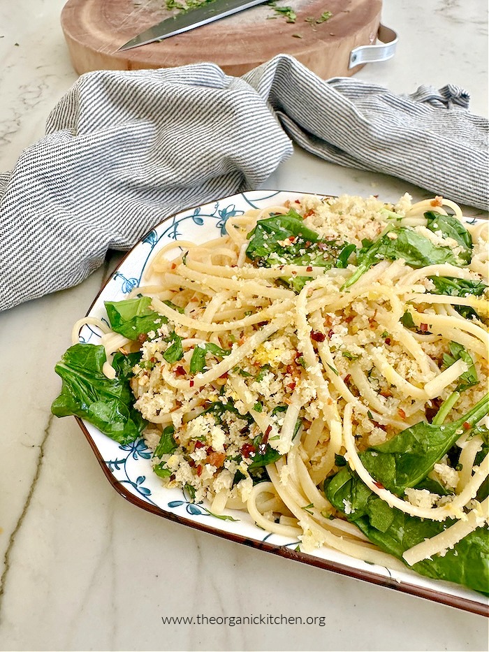 Browned Butter Linguine with Crispy Breadcrumbs on blue and white plate with striped dish towel and cutting board in the background