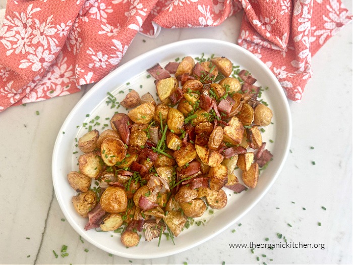 Air Fryer Potatoes with Bacon (Whole30) garnished with chives, on white plate with red dish towel above