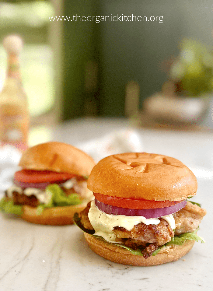 Best Fried Chicken Sandwich: two chicken burgers on white counter with tabasco in the background