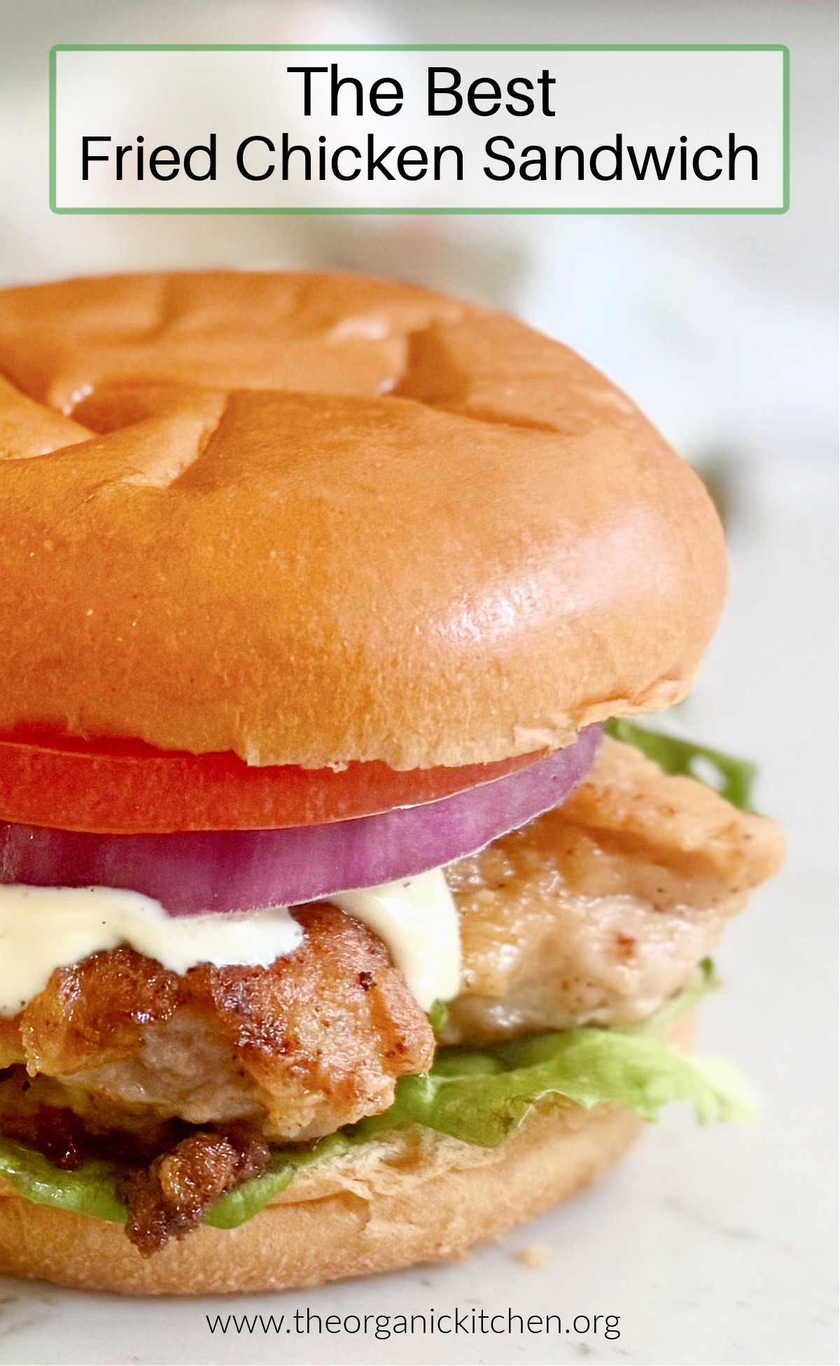 Best Fried Chicken Sandwich with ranch, lettuce, tomato and red onion on white marble surface