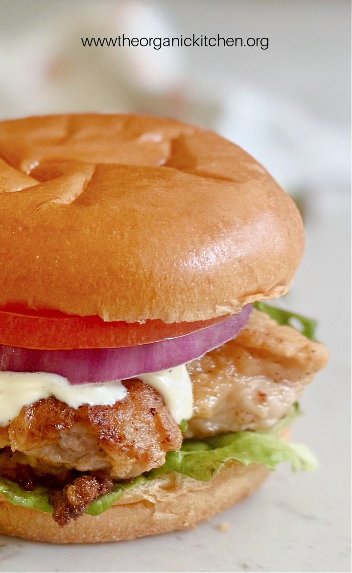 A chciken sandwich with bun and ranch dressing on white surface. 15 Healthy Chicken Thigh Recipes