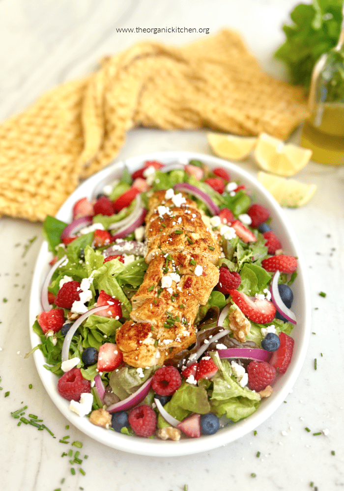 Chicken and Berry Salad on white plate set on white counter with chives, a yellow dish towel and basil in the background