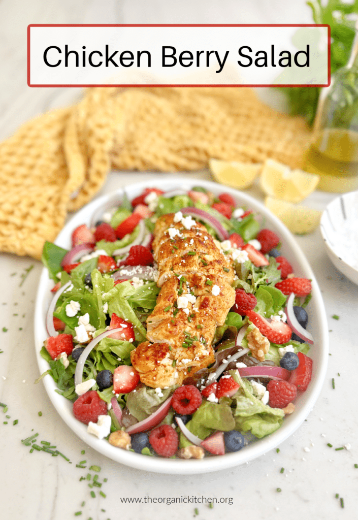 A sliced grilled chicken breast on top of greens and berries on white plate