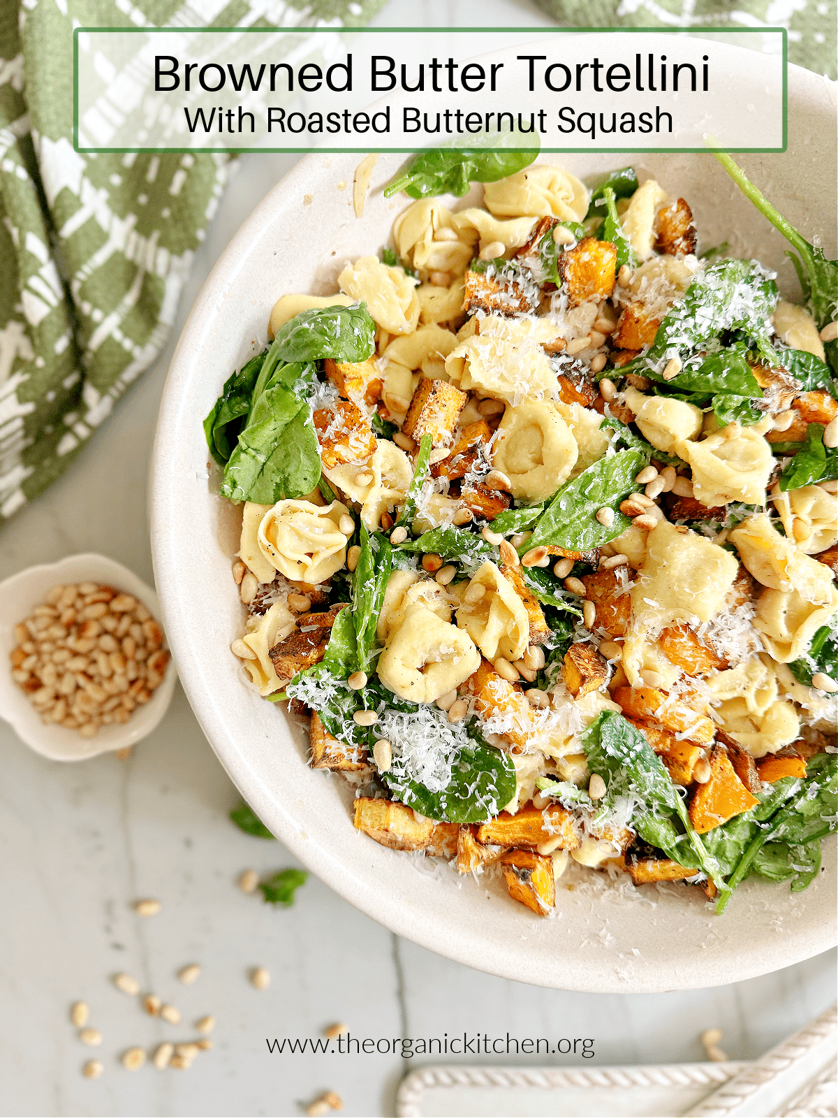 Browned Butter Tortellini with Roasted Butternut Squash in a white bowl with green and white dish towel and bowl of pine nuts in background