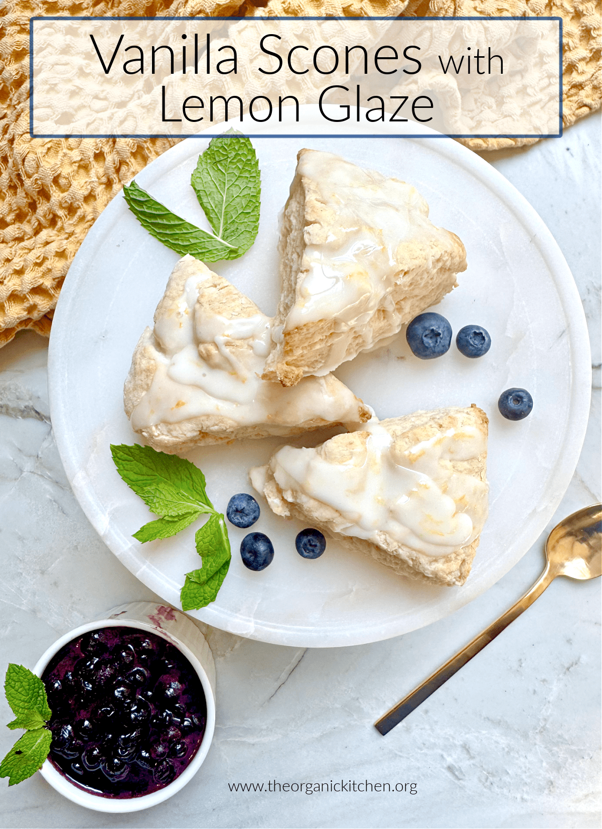 Vanilla Scones with Lemon Glaze Vanilla Scones with Lemon Glaze garnished with mint and blueberries on white plate with a bowl of blueberry compote and yellow dish towel in the background