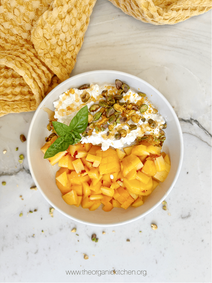 Peaches with Zesty Cottage Cheese garnished with basil on white counter with yellow dish towel above