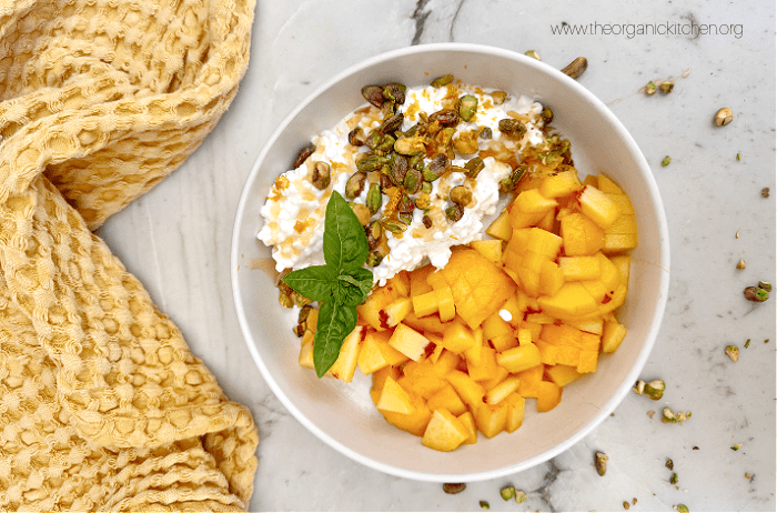 Peaches with Zesty Cottage Cheese ina white bowl set on white counter with yellow dish towel to the left