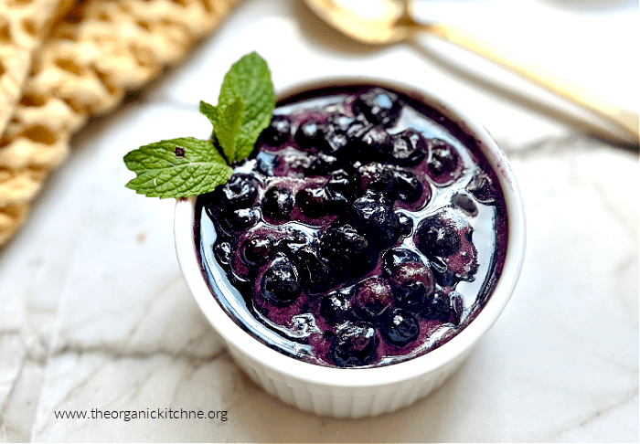 Easy Blueberry Compote Easy Blueberry Compote garnished with mint in a small white bowl set on a white counter with gold spoon in background