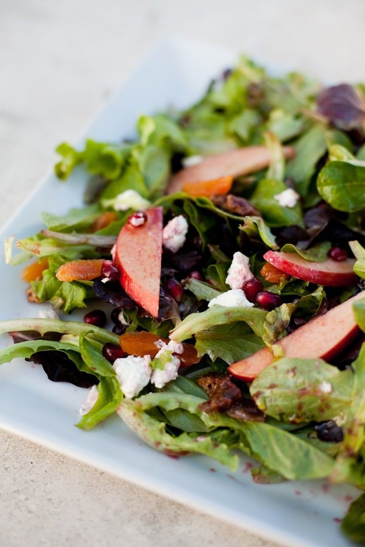 Green salad with apples and pomegranate seeds and feta on white plate