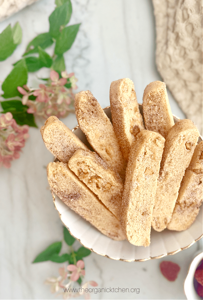 White Chocolate Biscotti in a bowl on marble counter with flowers in the background