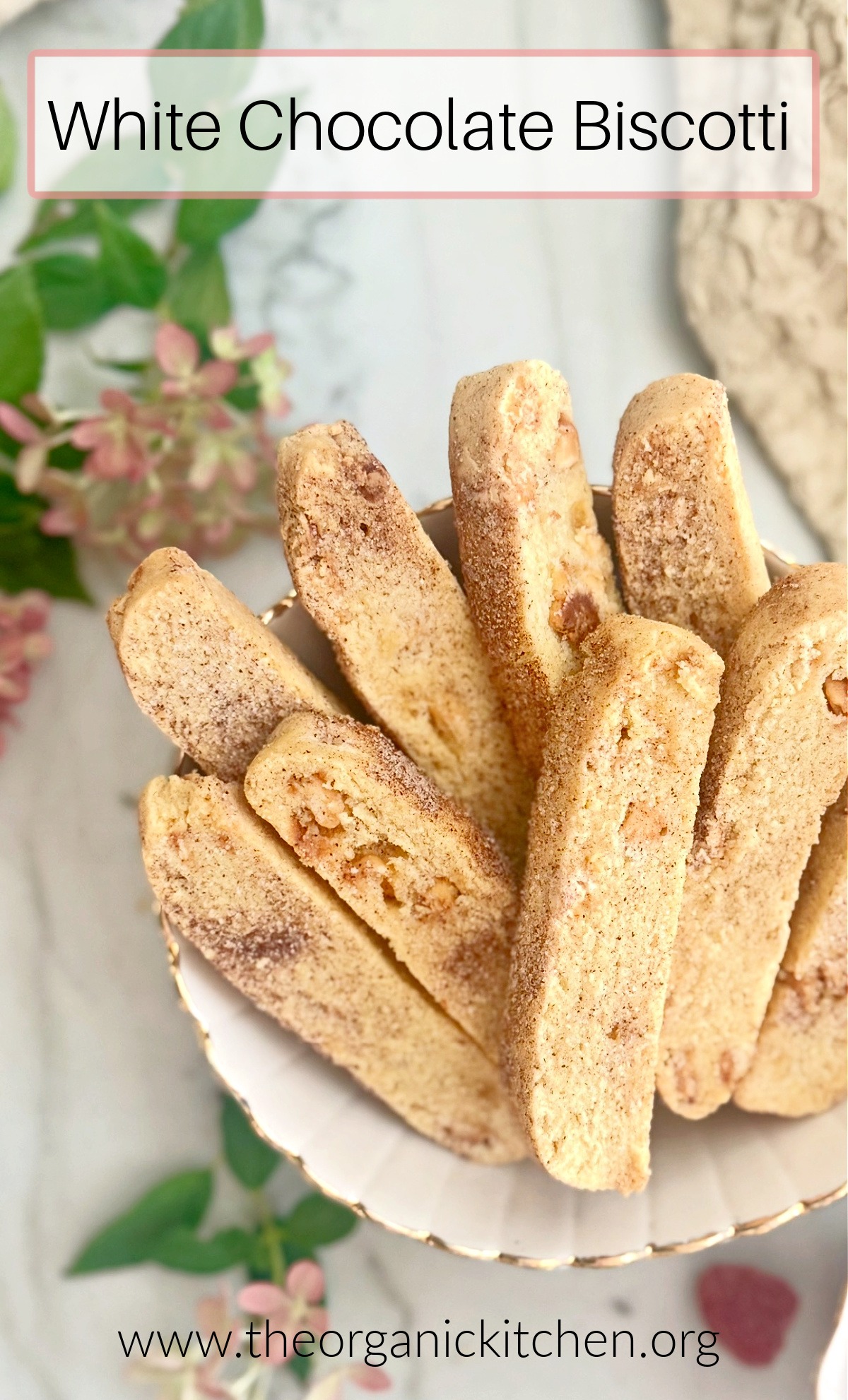 White Chocolate Biscotti in a bowl with flowers, raspberries and dish towel in background