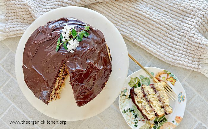 Italian Cream Cake with Chocolate Ganache Italian Cream Cake with Chocolate Ganache decorated with flowers on a cake plate with a slice of cake on a dish