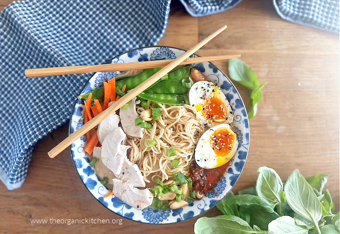 Easy Ramen with Chicken and Vegetables in blue and white bowl surrounded by basil, a blue dish towel and chop sticks