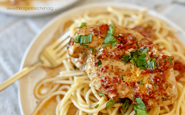 Marry Me Chicken garnished with basil on a bed of pasta on a white plate with gold fork