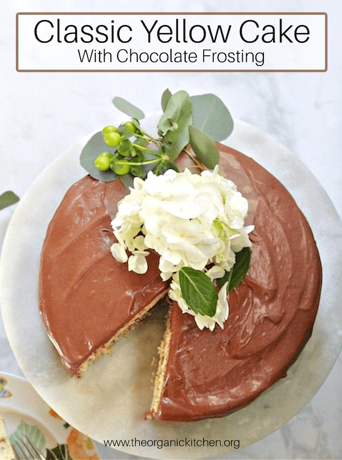 Classic Yellow Cake with Chocolate Frosting with flowers on top on a white marble cake plate