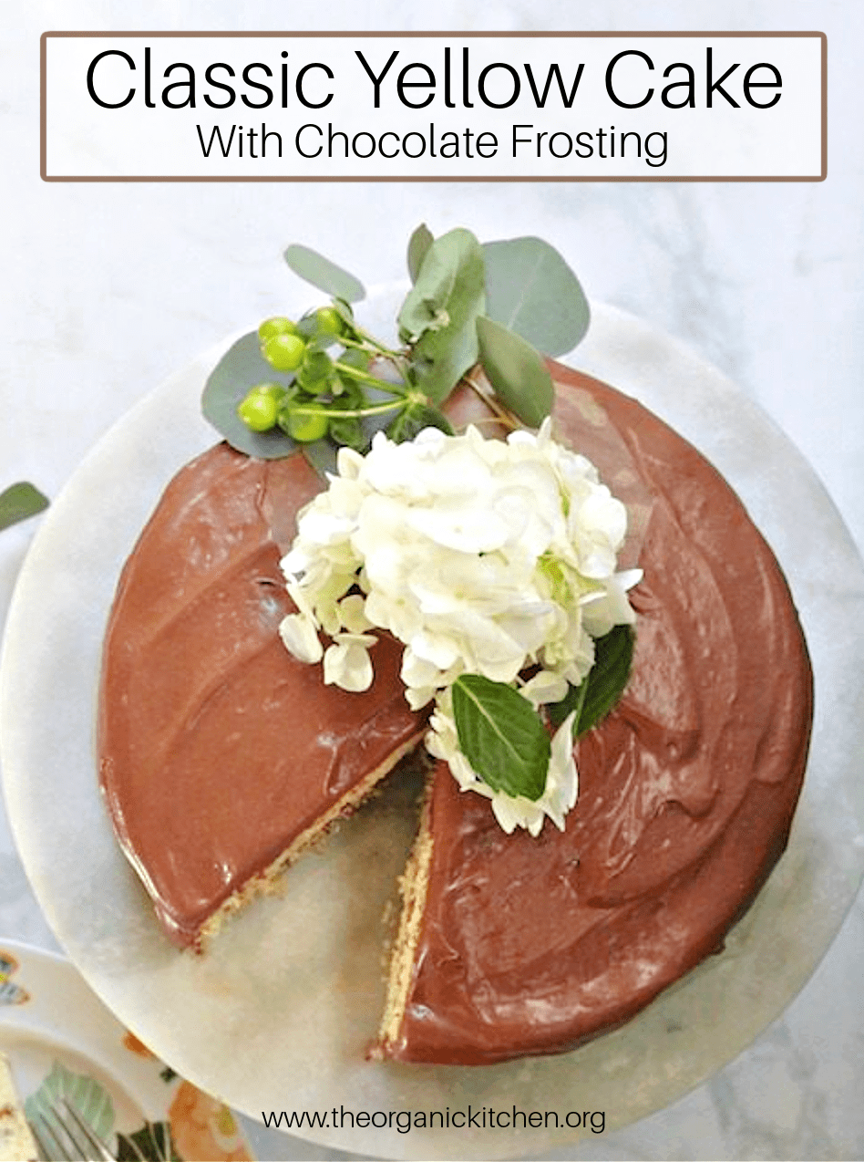 Classic Yellow Cake with Chocolate Frosting decorated with flowers and leaves, on a marble cake plate