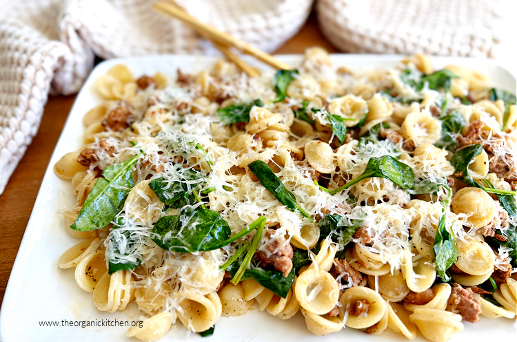 Pasta with Italian Sausage and Spinach t Pasta with Italian Sausage and Spinach tossed with parmesan cheese on white platter with gold serving spoons