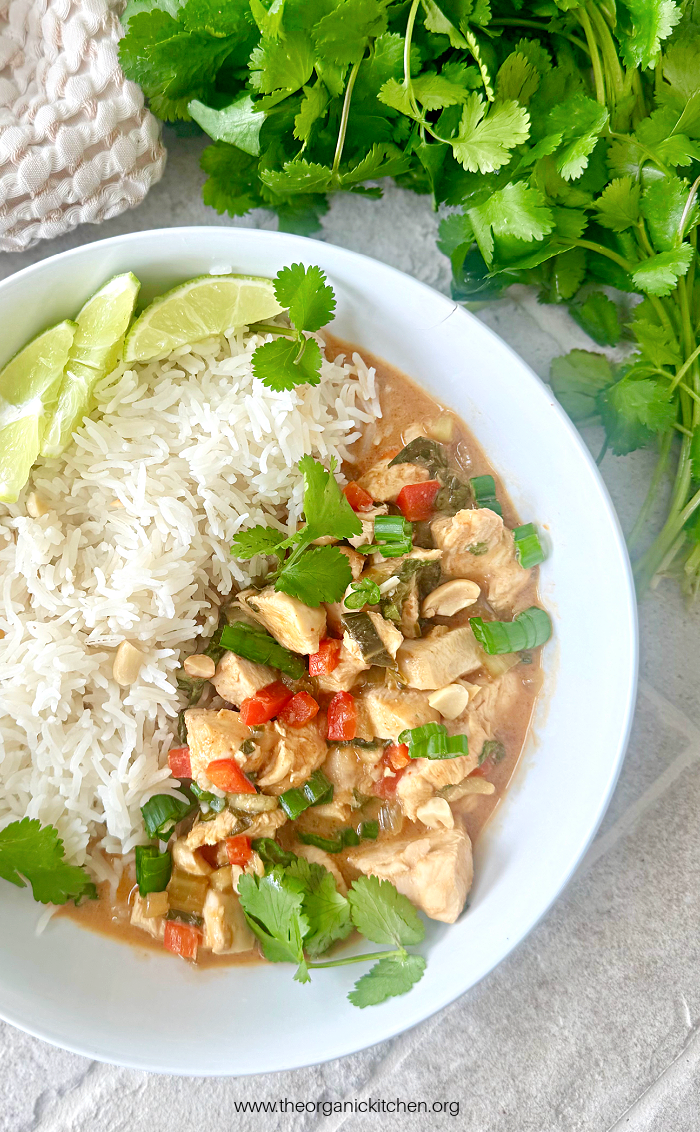 Asian Chicken and Rice Bowls garnished with herbs, lime wedges and peanuts on brick surface
