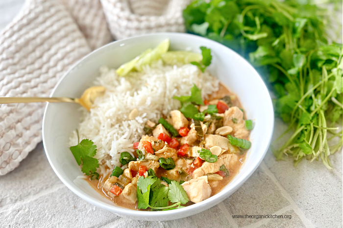 Asian Chicken and Rice Bowls with gold spoon, garnished with peanuts and cilantro, with herbs and dish towel in the background