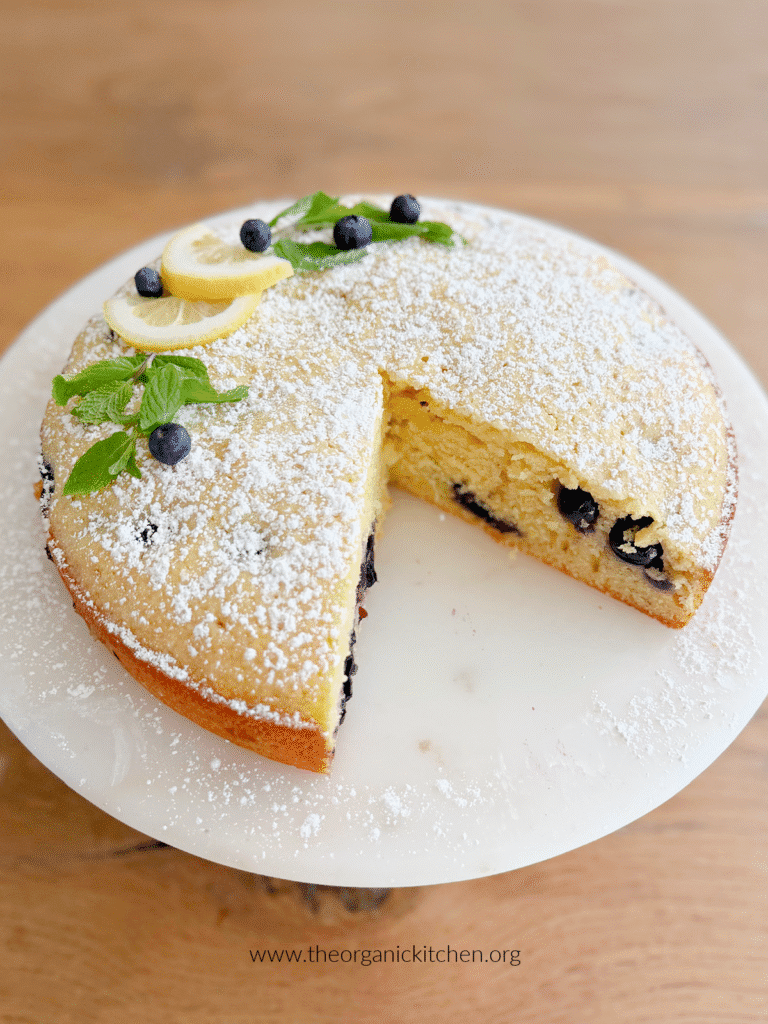 Lemon Blueberry Olive Oil Cake Lemon Blueberry Olive Oil Cake garnished with mint and blueberries on white cake plate set on wood tables