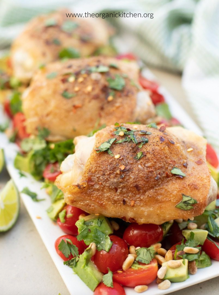 Spicy Lime Chicken thighs on top of an avocado ad tomato salad on white plate. 15 Healthy Chicken Thigh Recipes