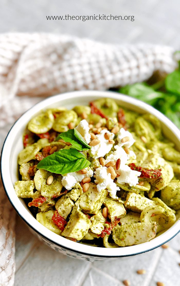 Chicken Pesto Orecchiette Chicken Pesto Orecchiette garnished with basil and su dried tomatoes in bowl with dish towel and basul in background
