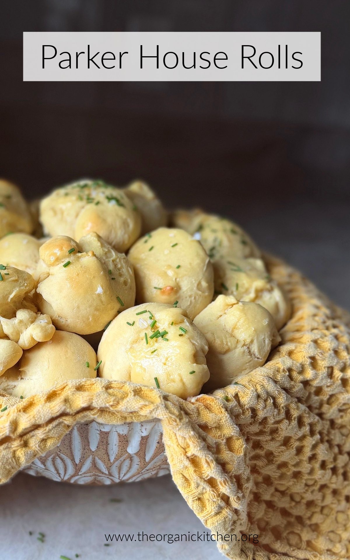 Parker House Rolls brushed with butter and garnished with chives in a bowl with yellow dish towel