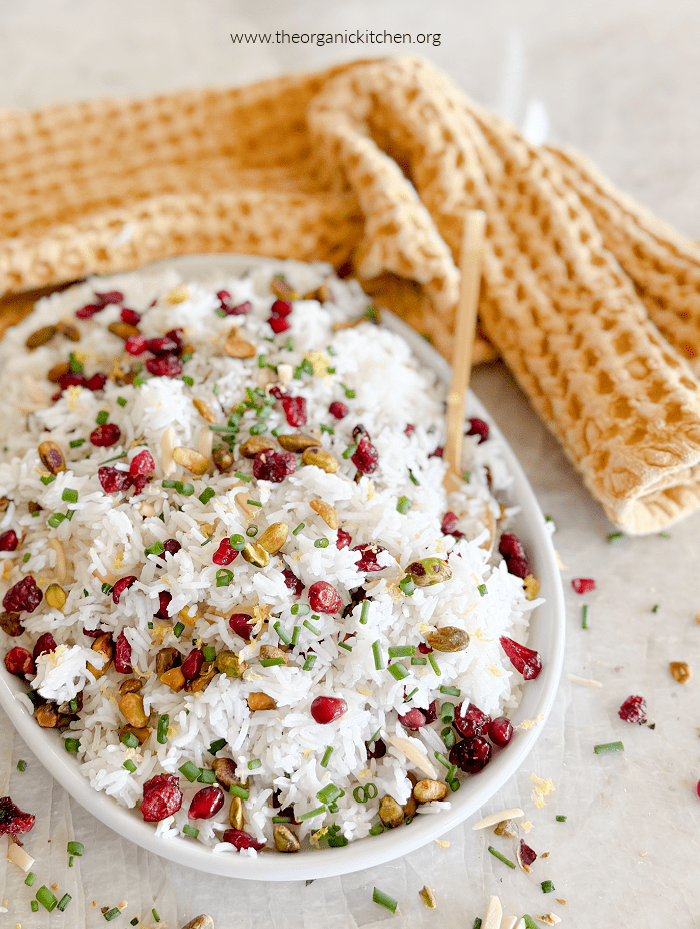 Easy Jeweled Rice garnished with dried fruit, herbs and nuts on white plate with yellow towel in the background