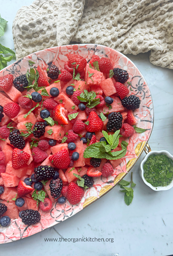 20 Easy Summer Side Dishes A pink platter filled with berries and topped with mint on marble table with a small bowl of lime juice and mint