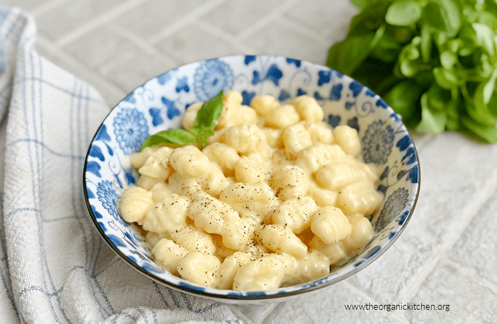 Three Cheese Gnocchi in a blue and white bowl with a dish towel and a bunch of basil in background