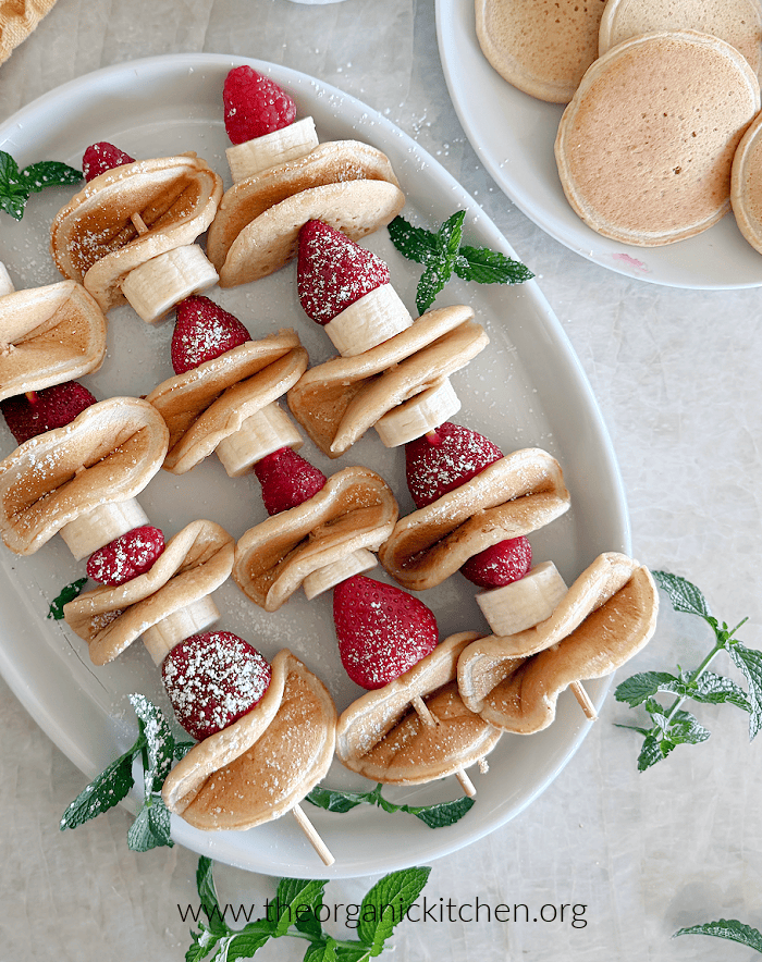 Pancake Fruit Skewers Three Pancake Fruit Skewers sprinkled with confectioners sugar and scatter with mint on white platter