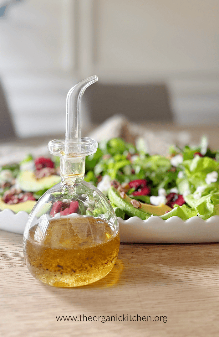 Easy White Balsamic Vinaigrette in a glass bottle in front of a colorful salad on a white plate
