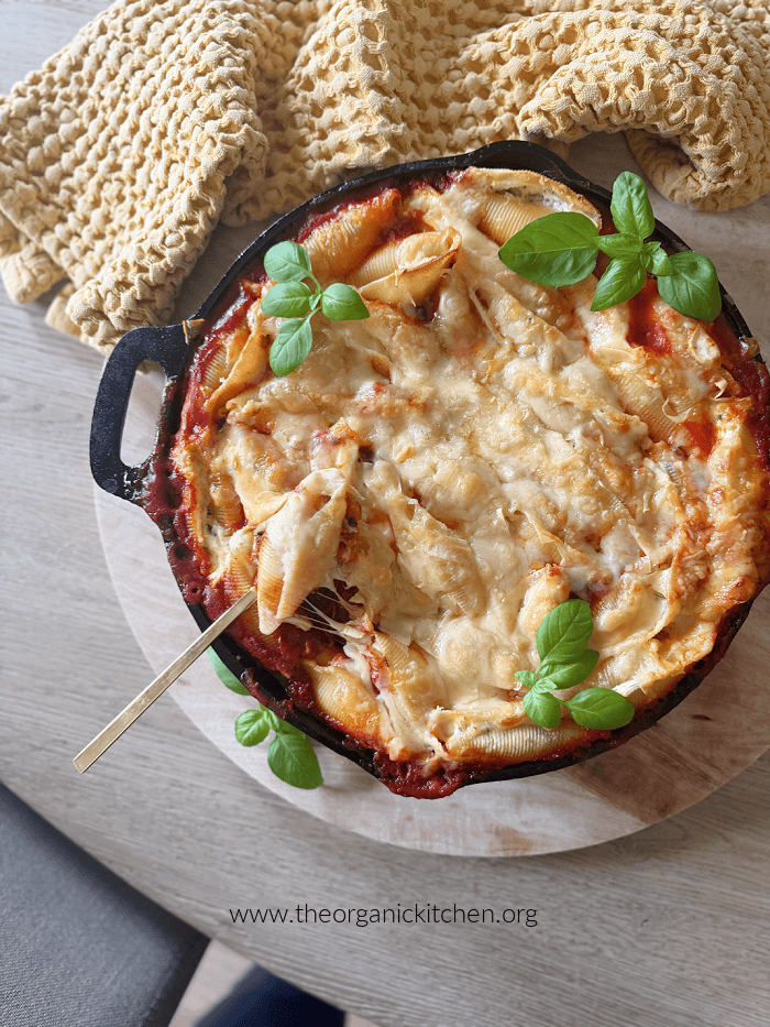Three Cheese Stuffed Shells A cast iron skillet with Three Cheese Stuffed Shells garnished with basil on wooden table