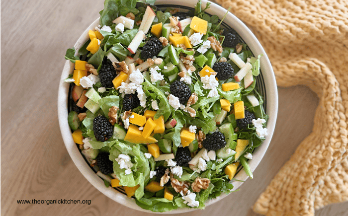 Easy Honey Vinaigrette A green salad with goat cheese, blackberries, mangoes and walnuts with Easy Honey Vinaigrette in white bowl