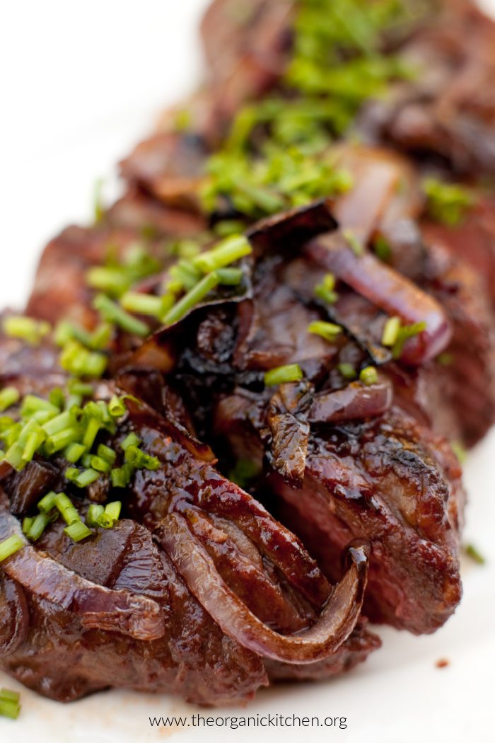Tri-tip steak garnished with caramelized onions and chives on white plate as part of 10 Delicious Grilling Recipes