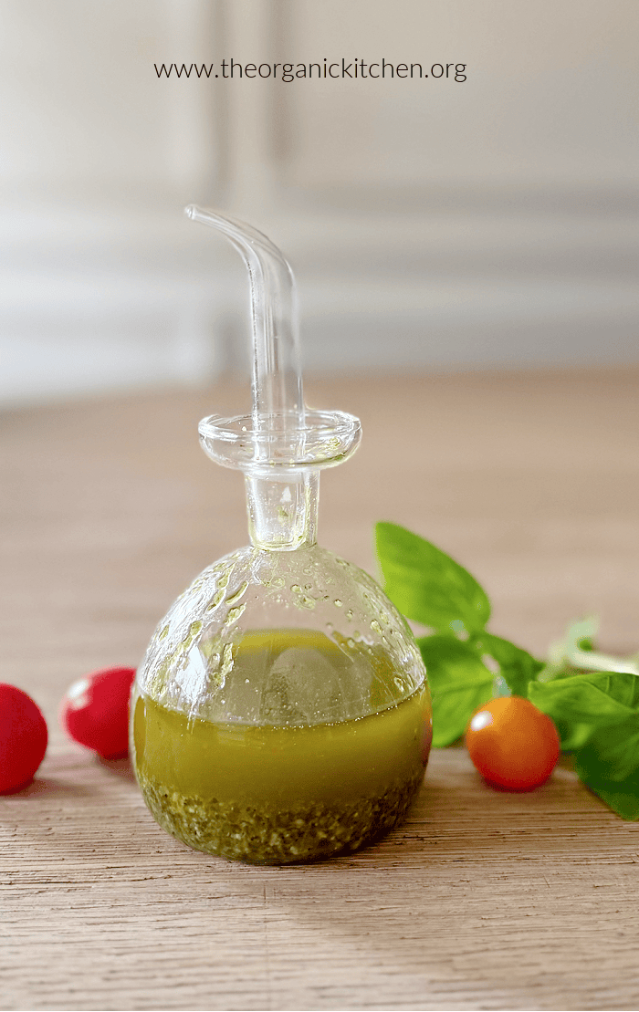 Tomato Burrata Salad with Basil Vinaigrette A small bottle of basil vinaigrette on a table, surrounded by cherry tomatoes and basil leaves