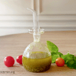 Basil Vinaigrette in a small glass bottle with cherry tomatoes and basil leaves in the background