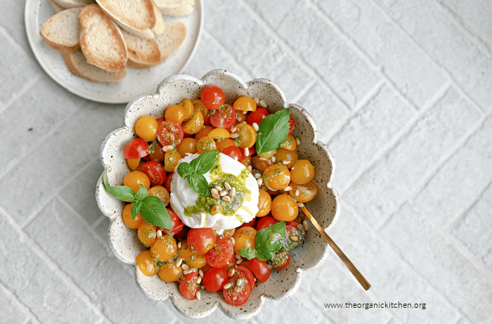 Tomato Burrata Salad with Basil Vinaigrette Tomato Burrata Salad with Basil Vinaigrette garnished with pine nuts in a white bowl with scalloped edges
