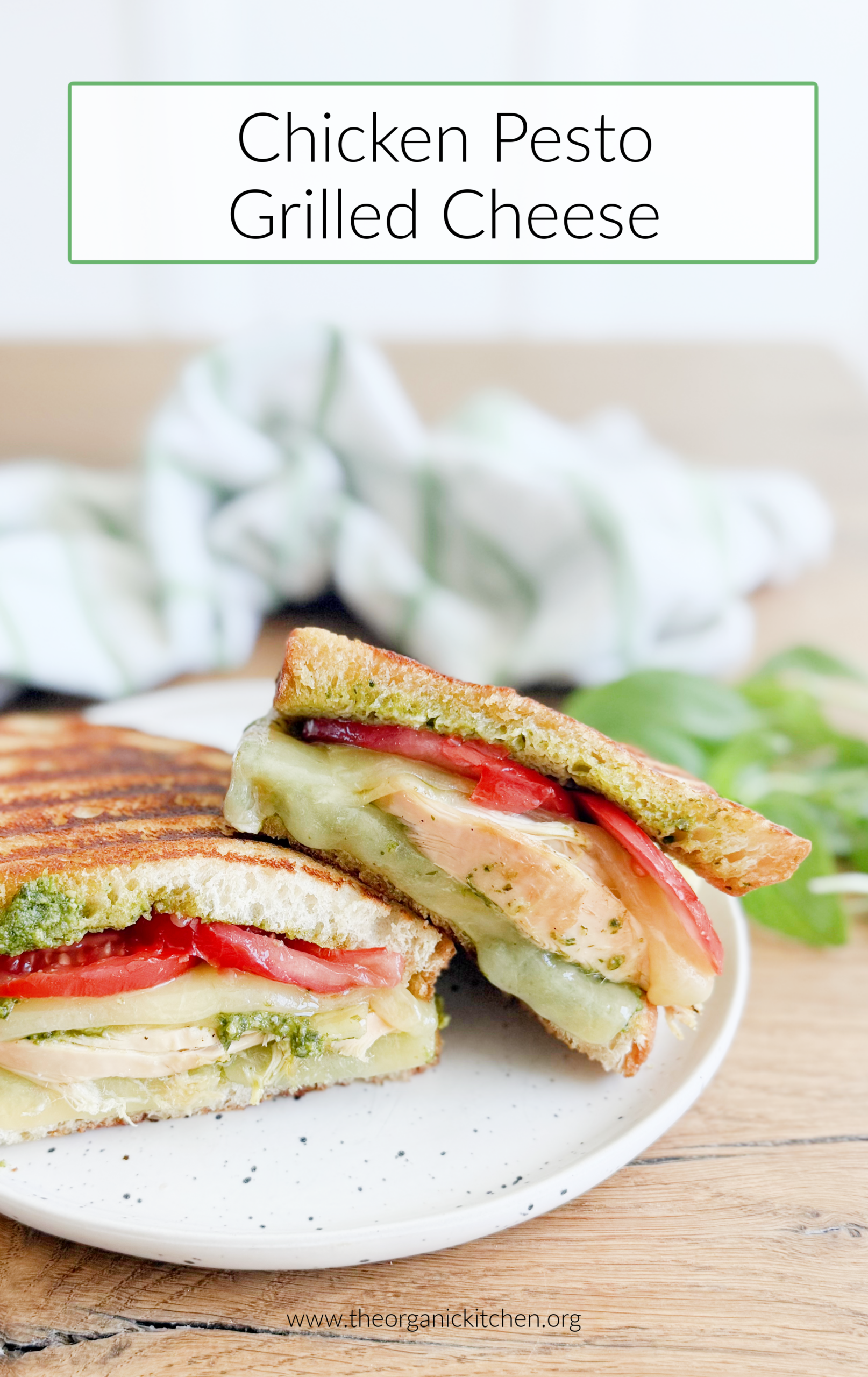 Two stacked Chicken Pesto Grilled Cheese sandwiches on a black and white plate with herbs and a green and white dish towel in the background