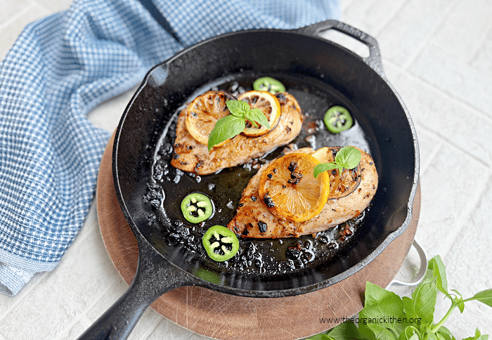 Spicy Lemon Basil Chicken Breasts- (Whole30, Low Carb) Two cooked chicken breasts garnished with herbs, lemon slices and peppers in black skillet
