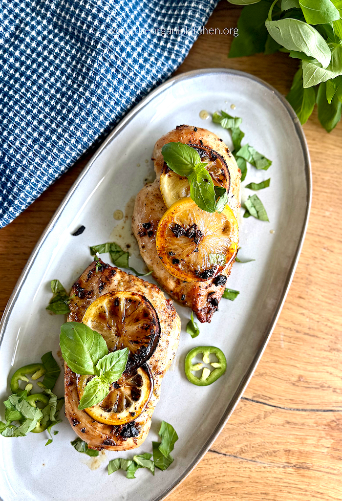 Spicy Lemon Basil Chicken Breasts- (Whole30, Low Carb) Spicy Lemon Basil Chicken Breasts- (Whole30, Low Carb) garnished with lemon, herbs and peppers on a grey plate with blue and white dish towel in the background
