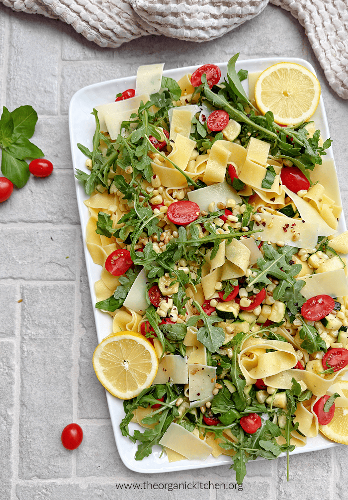 Delicious Summer Pasta Salad with tomatoes, arugula , parmesan and lemon slices on white platter