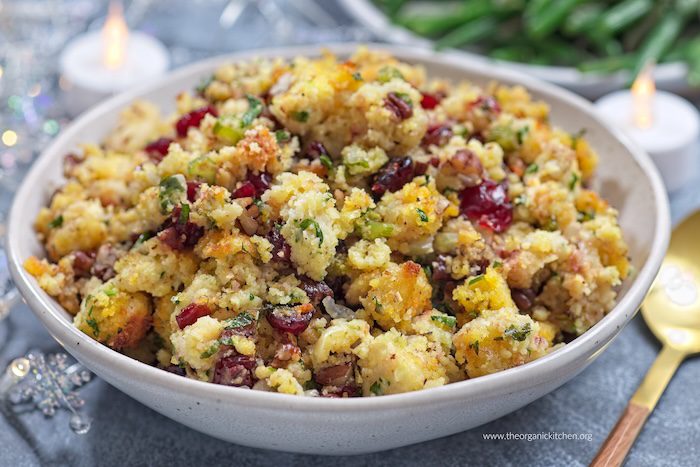 Delicious Buttery Herb Holiday Stuffing Delicious Herb Butter Holiday Stuffing with cranberries in a white bowl with a gold spoon and candle in the background